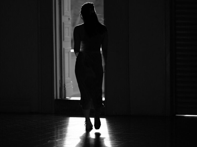 Shadowy silhouette of a woman walking towards an open door with natural light.