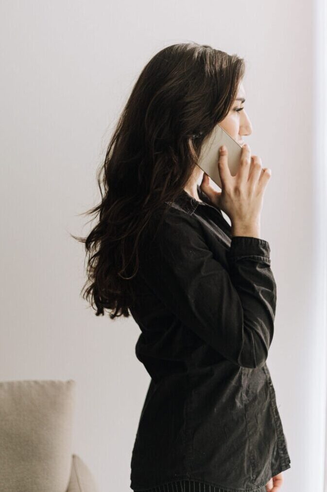 A woman engaged in a phone call in a well-lit office, wearing a black outfit.